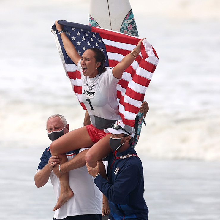 Carissa Moore celebrates on her surfboard after winning the Gold Medal match in Women's Surfing at the Tokyo 2020 Olympic Games.